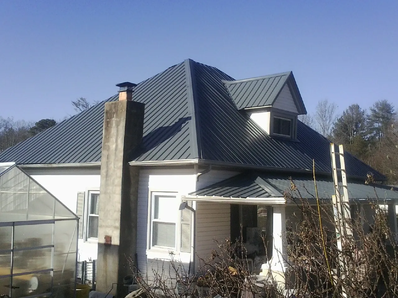 Dark blue standing seam metal roof on a white farmhouse with dormer — Slate & Tile Roof Repair by Roofing Brothers in Demorest