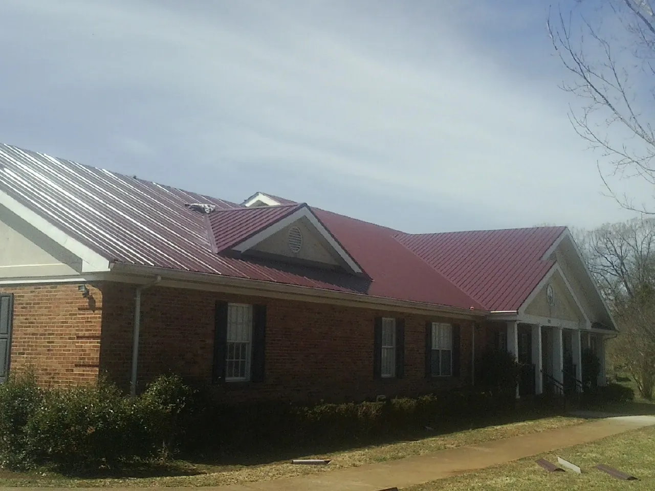 Red metal roof with gabled entries on a long brick building, from a Hail Damage Roof Repair job in Demorest