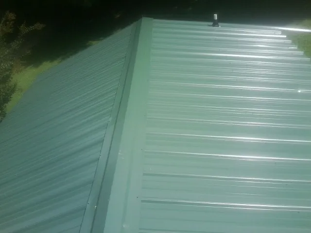 New green metal panels meeting at the ridge of a roof — Flat Roof Repair work by our crew in Demorest