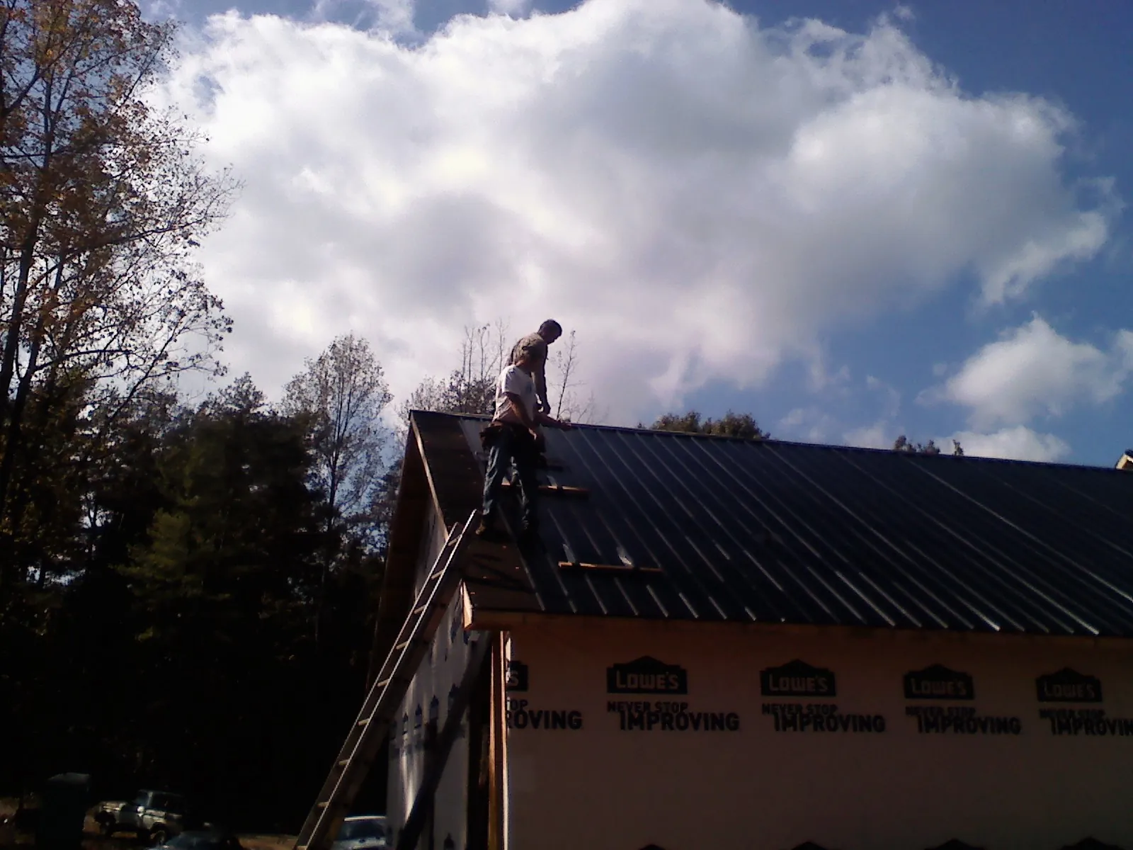 Roofer fastening dark metal panels high against a cloudy sky, from a Roof Inspection job in Demorest